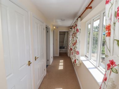 A hallway with three white doors on the left and windows with floral curtains on the right at Pheasant Cottage in Minster Lovell