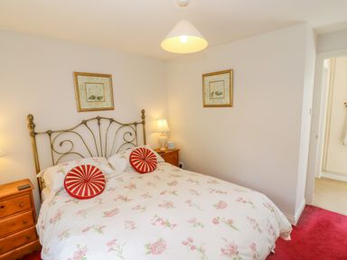 A bedroom with a double bed floral bedding and red circular cushions wooden bedside tables lamps and framed pictures at Pheasant Cottage in Minster Lovell