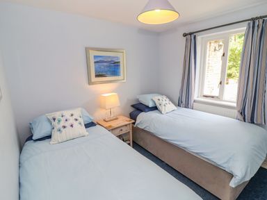 A bedroom with two single beds a nightstand lamp window and striped curtains at Pheasant Cottage in Minster Lovell