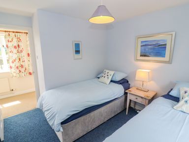A bedroom with two single beds a wooden nightstand with a lamp and framed art on the walls at Pheasant Cottage in Minster Lovell