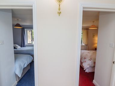 Two bedrooms with beds seen through two doorways at Pheasant Cottage in Minster Lovell
