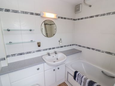 A bathroom with a sink cabinet mirror bathtub and decorative tile trim at Pheasant Cottage in Minster Lovell