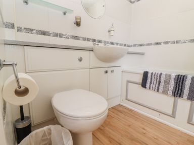 A bathroom with a toilet, sink, bathtub, striped towel, toilet paper holder, and wooden floor at Pheasant Cottage in Minster Lovell