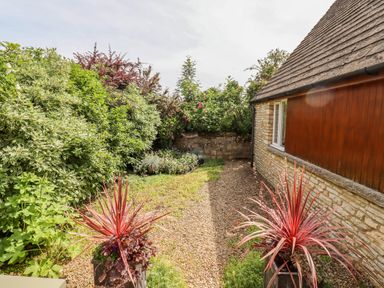 A garden with gravel pathway bordered by plants and a stone house wall at Pheasant Cottage in Minster Lovell