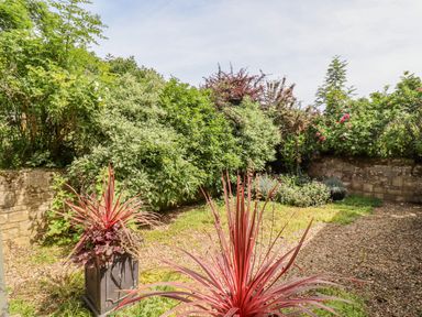 A garden with shrubs flowers and two rectangular plant pots at Pheasant Cottage in Minster Lovell