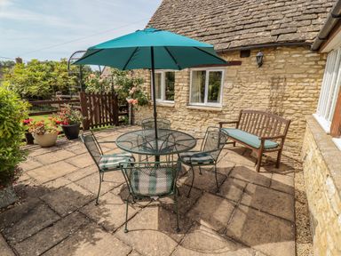 An outdoor patio with a circular metal table and four chairs with cushions and a teal umbrella at Pheasant Cottage in Minster Lovell
