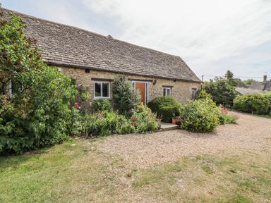 Stone cottage with wooden door surrounded by garden plants and gravel driveway at Pheasant Cottage in Minster Lovell