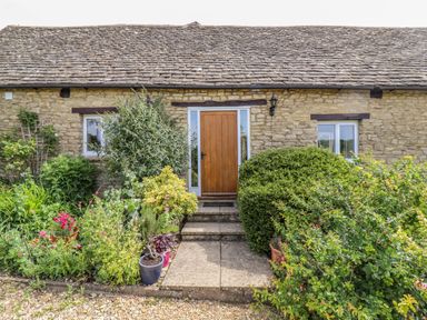 Stone cottage exterior with wooden door and surrounding plants at Pheasant Cottage in Minster Lovell