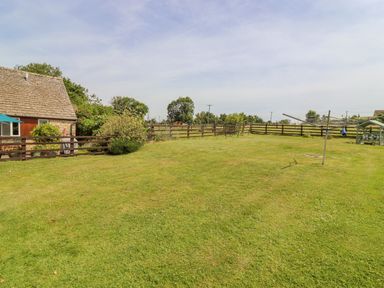 A backyard with a wooden fence a rotary clothesline and a stone house with a tiled roof at Pheasant Cottage in Minster Lovell