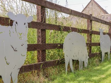 Metal sheep silhouettes attached to a wooden fence with wire mesh in a grassy area