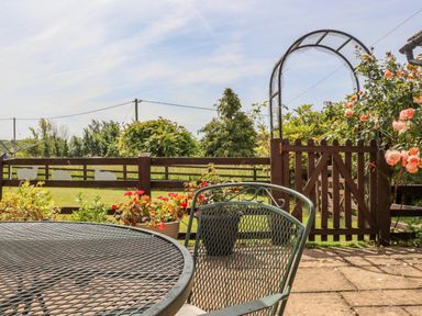 A patio with metal table and chair overlooking a garden gate with flowers at Pheasant Cottage in Minster Lovell