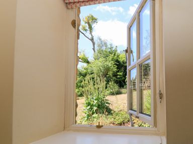 A view of plants and grass through an open window at Upper Mill Barn, Coln St Aldwyns, near Bibury