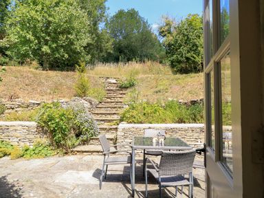 A garden with a table and chairs overlooking stone steps at Upper Mill Barn, Coln St Aldwyns, near Bibury