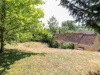 A garden with trees and a building at Upper Mill Barn in Coln St Aldwyns near Bibury