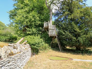 A treehouse with a wooden ladder and stone wall at Upper Mill Barn, Coln St Aldwyns, near Bibury