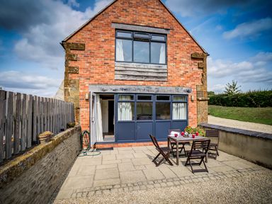 An outdoor patio area with a table and four chairs in front of a brick house with blue windows and doors at Top Barn in Chipping Norton