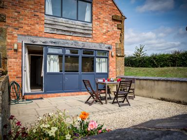 An outdoor patio area with a table and four chairs in front of a brick building at Top Barn in Chipping Norton
