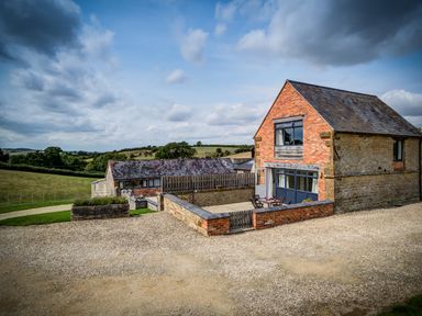 A two-story brick and stone house with a patio and table in a rural area at Top Barn in Chipping Norton