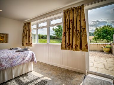 A bedroom with a bed folded towels window curtains and a door leading outside at Top Barn in Chipping Norton