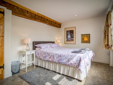 A bedroom with a double bed covered in patterned bedding two bedside tables with lamps a rug on tiled floor a framed picture on the wall and curtains at Top Barn in Chipping Norton