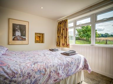 A bedroom with a patterned bedspread two folded towels a window with curtains and a framed picture on the wall at Top Barn in Chipping Norton