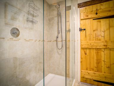 A tiled shower area with glass panels and a wooden door at Top Barn in Chipping Norton