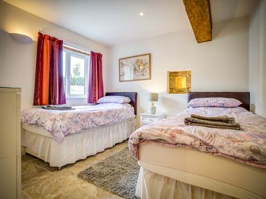 A bedroom with two single beds a nightstand with a lamp red curtains and a framed picture at Top Barn in Chipping Norton
