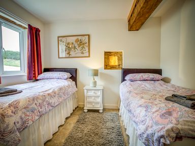 A bedroom with two single beds a window with curtains and a bedside table with a lamp at Top Barn in Chipping Norton