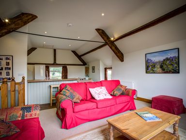 A living room with red sofas a wooden coffee table exposed ceiling beams and a kitchen counter at Top Barn in Chipping Norton