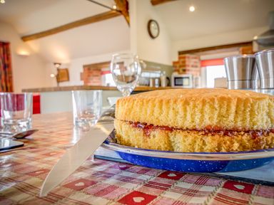 A sponge cake with jam on a plate on a table with glasses and a knife in a kitchen at Top Barn in Chipping Norton