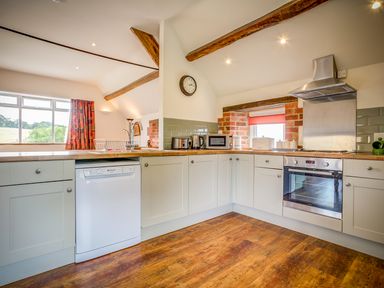A kitchen with white cabinets wooden countertops appliances and a window with red curtain at Top Barn in Chipping Norton