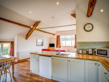 A kitchen with white cabinets a wooden countertop a dishwasher a sink toaster kettle microwave and a dining table with chairs near windows at Top Barn in Chipping Norton