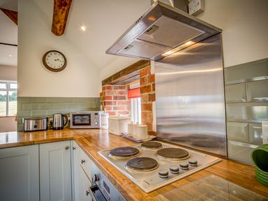 A kitchen with a stove cooker hob toaster kettle and microwave on wooden countertops at Top Barn in Chipping Norton