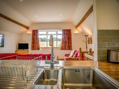 A kitchen sink with a drying rack and view of a living room with red sofas and a window with patterned curtains at Top Barn in Chipping Norton