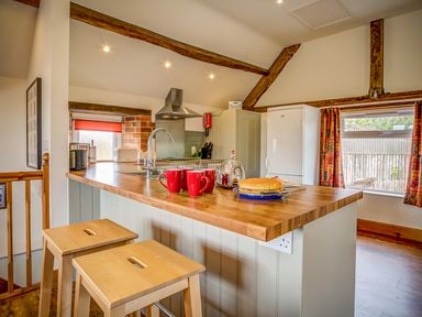 A kitchen with wooden countertop stools red mugs cake on a plate and exposed wooden beams at Top Barn in Chipping Norton