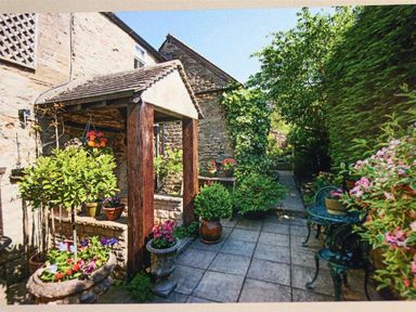A garden patio with stone walls potted plants and a small metal table with chairs at Pike Cottage in Stow-On-The-Wold