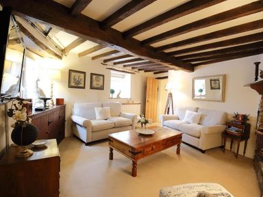A living room with wooden beams on the ceiling two white sofas a wooden coffee table and a floor lamp at Pike Cottage in Stow-On-The-Wold