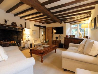 A living room with wooden ceiling beams a stone fireplace two beige sofas and a wooden coffee table at Pike Cottage in Stow-On-The-Wold