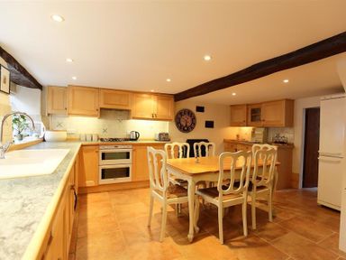 A kitchen with wooden cabinets a dining table with chairs a stove and a refrigerator at Pike Cottage in Stow-On-The-Wold