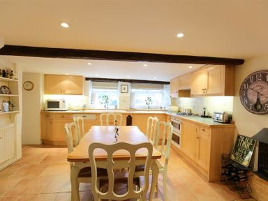 A kitchen with wooden cabinets a dining table with chairs and appliances at Pike Cottage in Stow-On-The-Wold