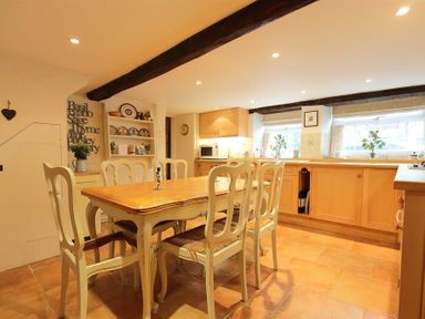 A kitchen with a wooden dining table and chairs wooden cabinets and shelves with dishes at Pike Cottage in Stow On The Wold