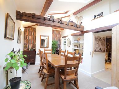 A dining room with wooden table and chairs wooden beams on ceiling and shelves with pictures at Pike Cottage in Stow-On-The-Wold