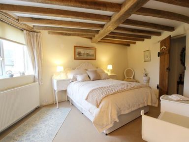 A bedroom with wooden ceiling beams a double bed bedside tables with lamps a chair and a wooden door at Pike Cottage in Stow-On-The-Wold