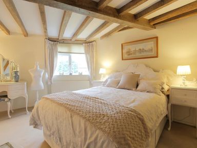 A bedroom with a large bed bedside tables lamps a window with curtains a vanity table and a mannequin at Pike Cottage in Stow-On-The-Wold