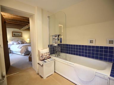 A bathroom with a bathtub with blue tiles and a view into a bedroom with a bed at Pike Cottage in Stow-On-The-Wold