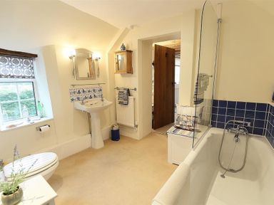 A bathroom with a bathtub, pedestal sink, toilet, window, and wooden door at Pike Cottage in Stow-On-The-Wold