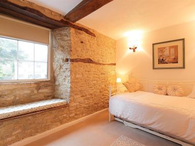 A bedroom with a daybed a window with a built in seat and stone walls at Pike Cottage in Stow-On-The-Wold