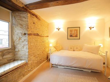 A bedroom with a bed window seat and exposed stone wall at Pike Cottage in Stow-On-The-Wold