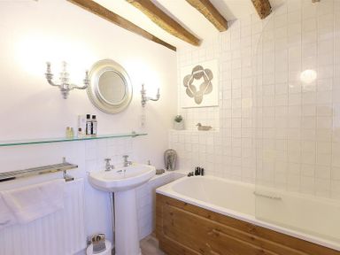 A bathroom with a sink and mirror above it and a bathtub with wooden paneling at Pike Cottage in Stow On The Wold