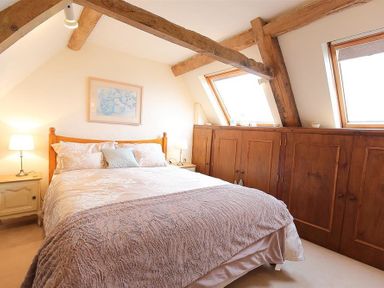 A bedroom with a double bed two bedside tables with lamps wooden cabinets and slanted windows at Pike Cottage in Stow-On-The-Wold